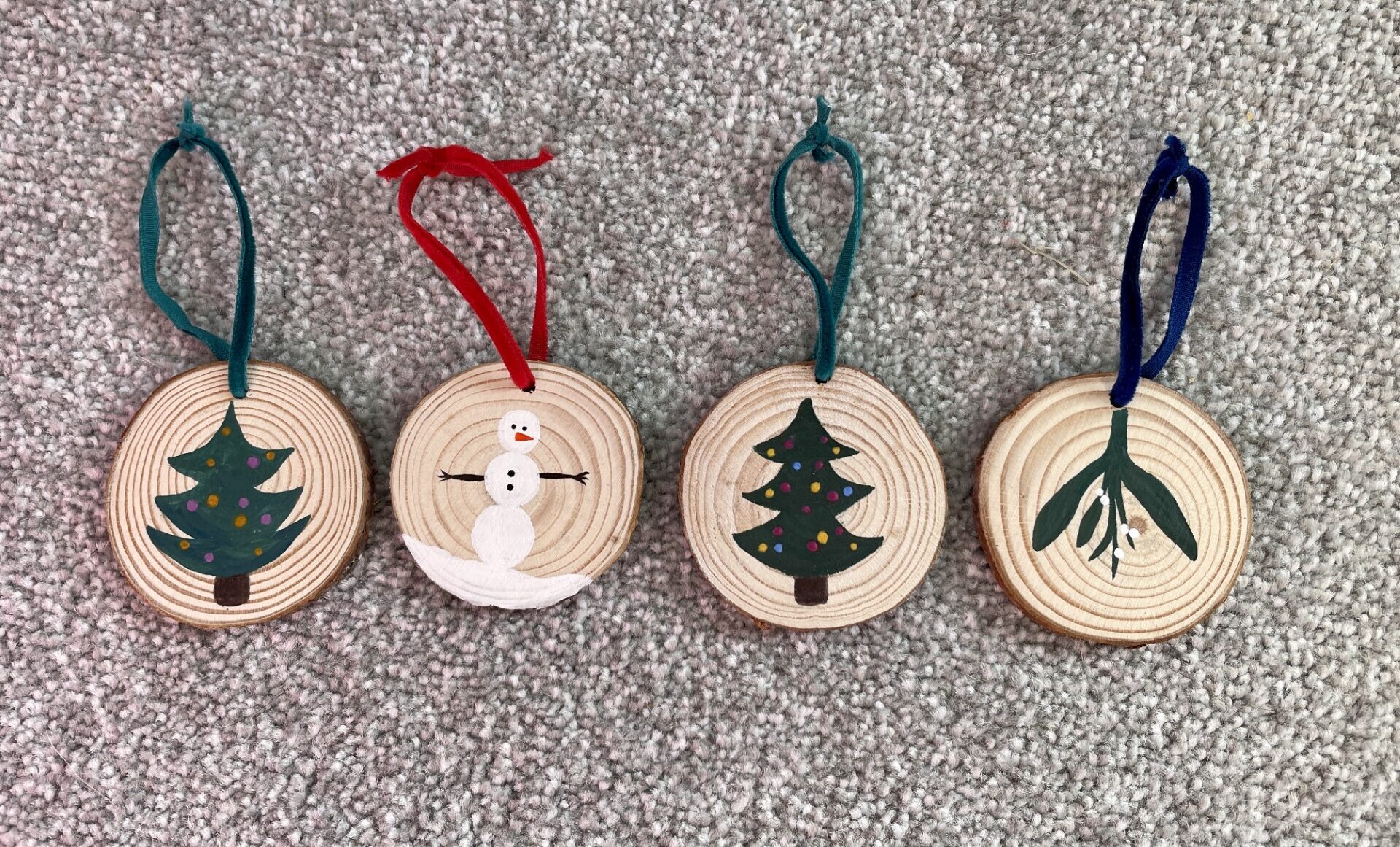 Four wooden ornaments with christmas trees on them.