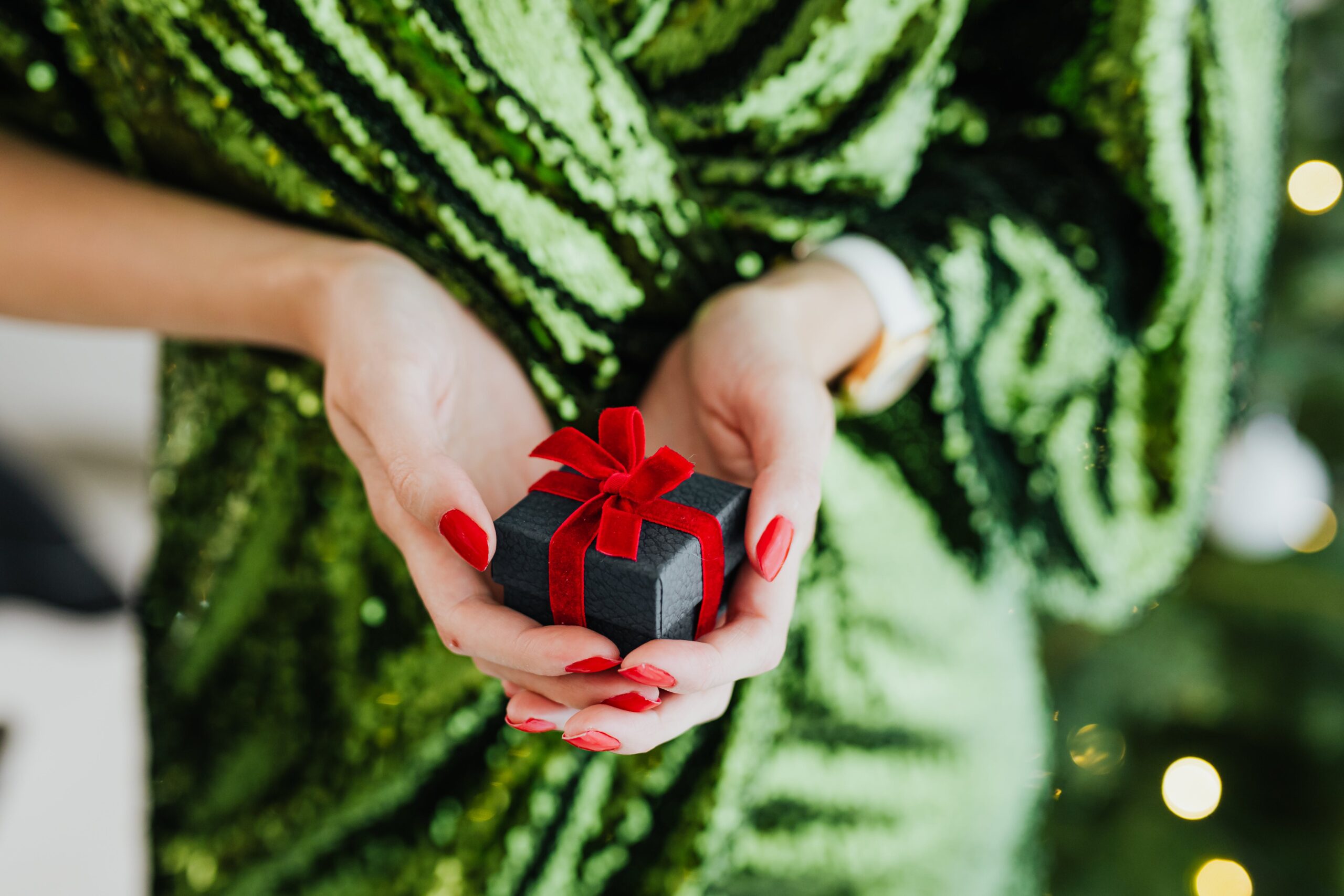 A woman is holding a gift box in front of a Christmas tree as part of an advent calendar surprise.