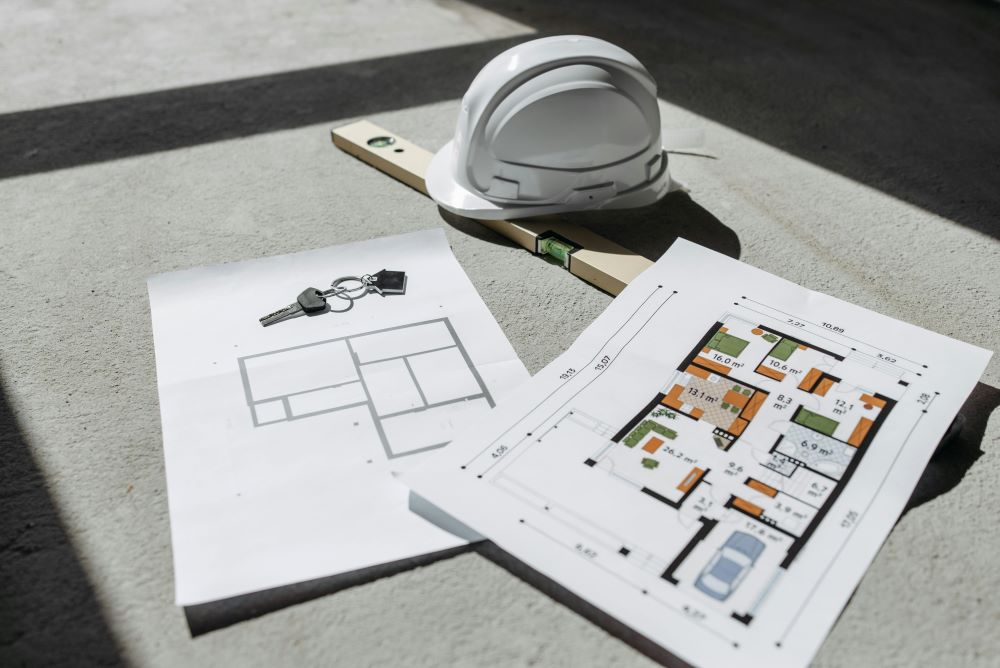 Construction plans with a hard hat, keys, and house survey on a concrete surface.