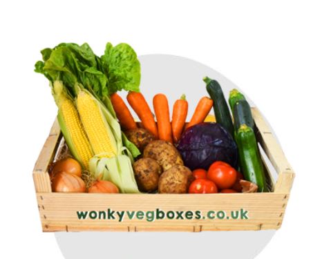 A wooden crate labeled "wonkyvegboxes.co.uk" contains various vegetables including lettuce, corn, carrots, zucchini, potatoes, onions, tomatoes, and a purple cabbage.