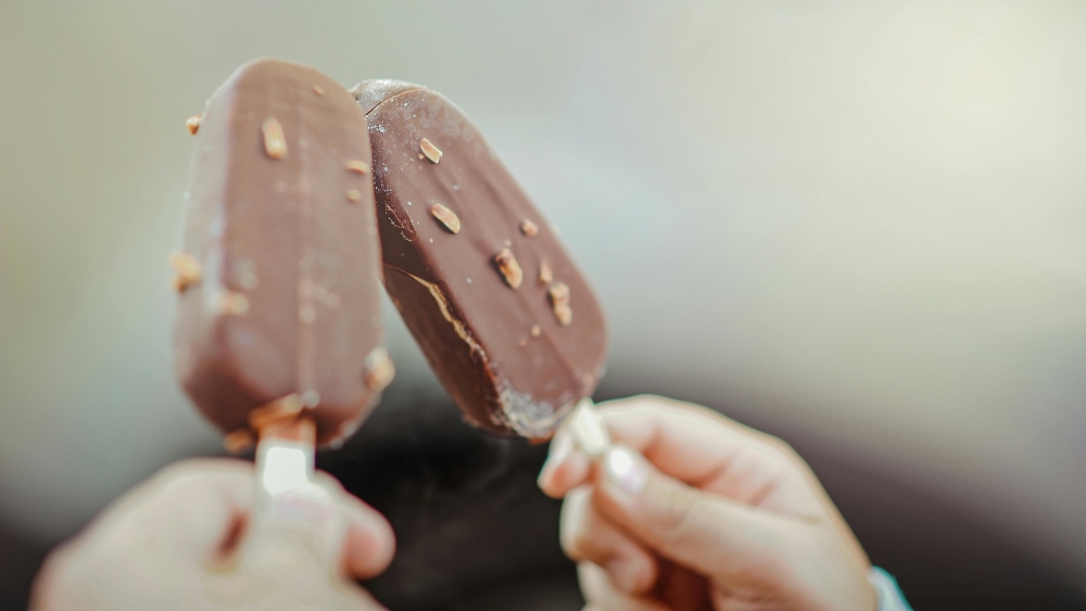 Two hands holding chocolate-covered ice cream bars with nuts up close.