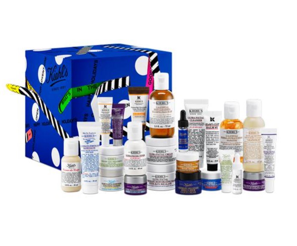 A large assortment of various skincare products from Kiehl's is displayed in front of a blue gift box with white polka dots.