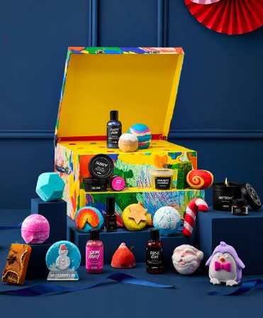 A colorful gift box with assorted bath and body products, including bath bombs, soaps, and lotions, arranged on a blue surface. A variety of shapes and colors create a festive display.