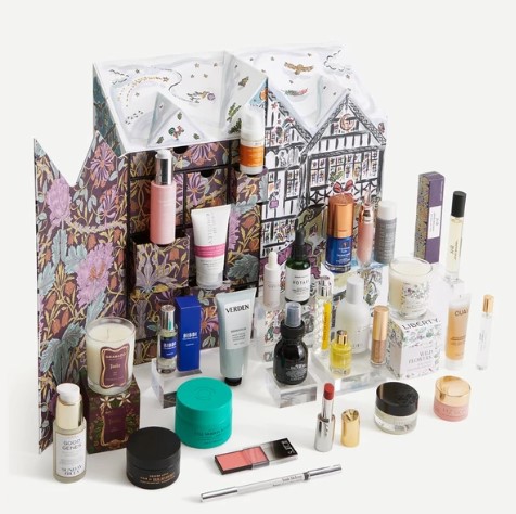 A collection of assorted skincare, makeup, and beauty products arranged around a decorated box with a floral pattern and illustrated buildings.