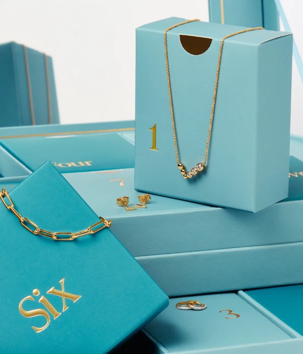 A collection of teal gift boxes numbered one through six, featuring various gold jewelry items including a necklace, bracelet, earrings, and ring.