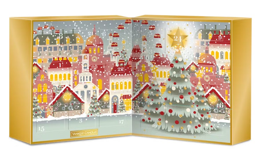 An open holiday advent calendar featuring a festive town and Christmas trees with numbered doors. Snowflakes fall over the scene.