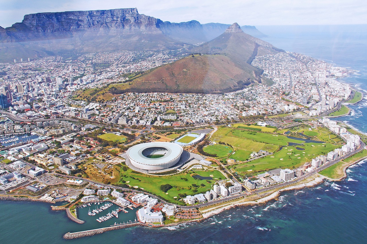 Aerial view of Cape Town, featuring a stadium, coastal area, and Table Mountain in the background.