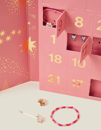 A pink advent calendar with open doors revealing jewelry items like earrings, a ring, a bracelet, and a pin.