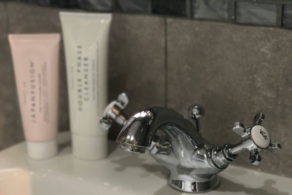 A chrome faucet is centered between two tubes of cream placed on a bathroom sink countertop.