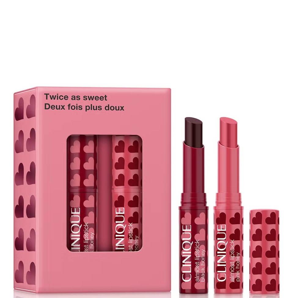 Two Clinique lipsticks, one dark and one pink, with heart-patterned packaging, alongside a matching pink box labeled "Twice as sweet.