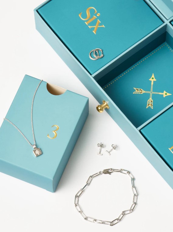 Jewelry set in blue boxes, including a necklace with a star pendant, hoop and stud earrings, and a chain bracelet, displayed on a white surface.