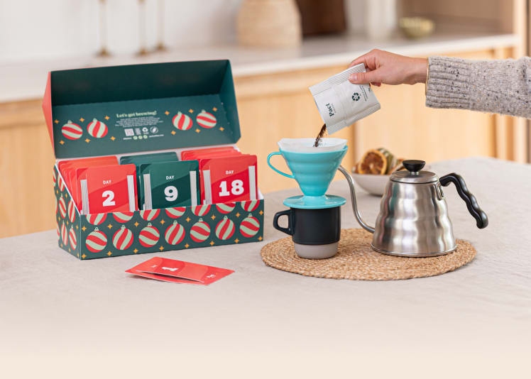 An open coffee advent calendar with many different blends inside, while a hand pours some into a cup.