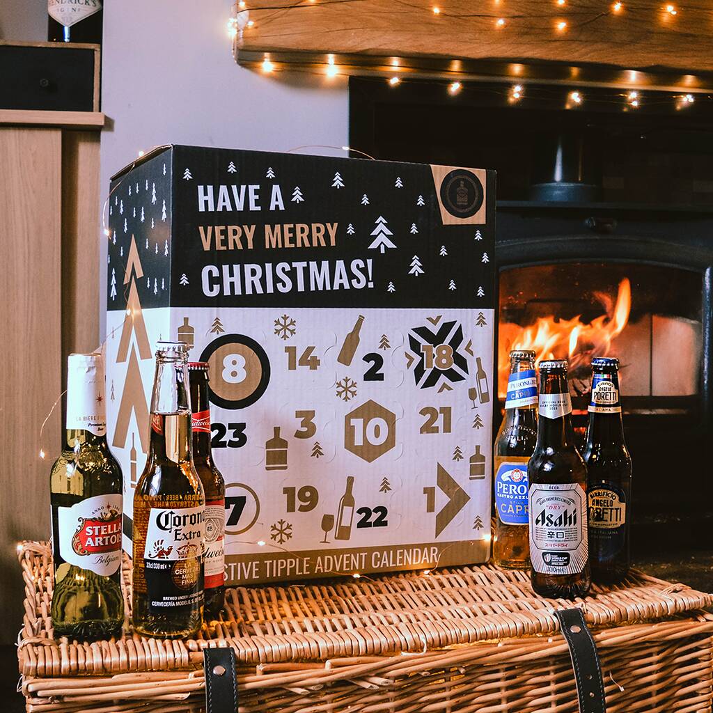 Assorted beer bottles on a wicker basket in front of a holiday-themed calendar and a lit fireplace.