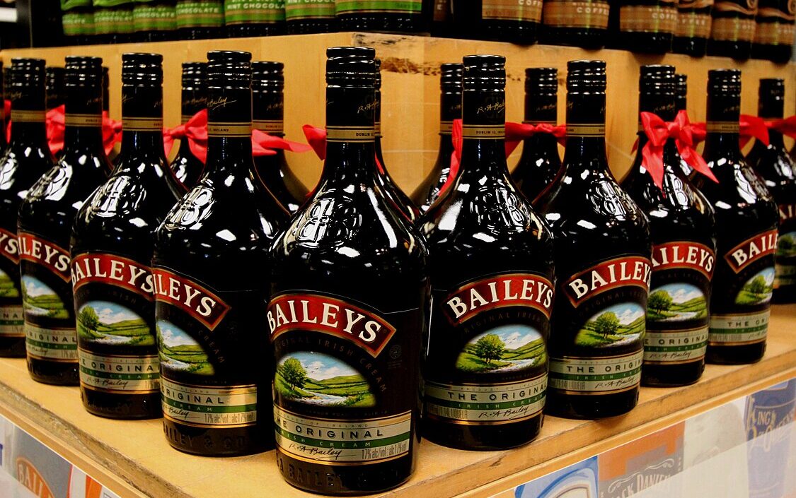 Bottles of Baileys Irish Cream and Chocolate Luxe, some adorned with red bows, are elegantly arranged on a store shelf. Discover the latest Baileys offers, like the cheapest 1-litre bottles available today.