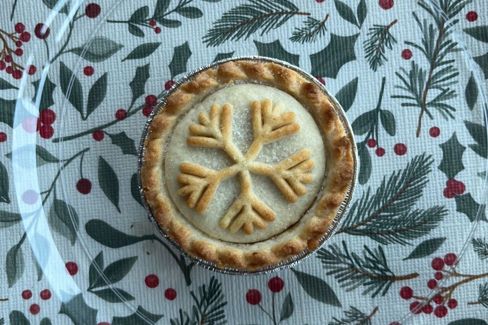 A pie with a snowflake pattern on top, placed on a festive tablecloth with pine and berry design.