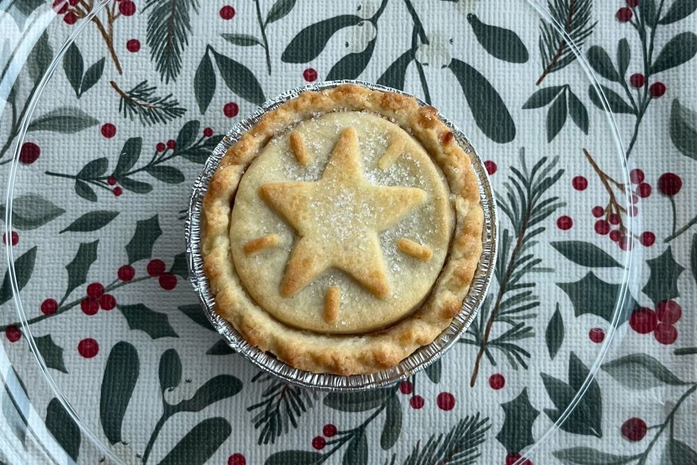 A pie with a star-shaped design on top sits on a festive tablecloth with green leaves and red berries.