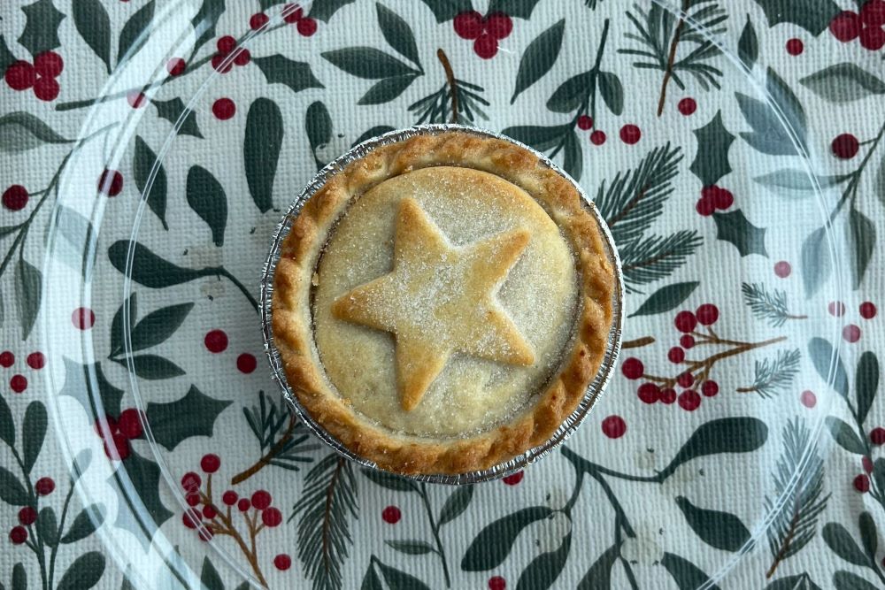 Round pie with a star-shaped crust on top, placed on a glass plate. The background features a festive pattern with holly leaves and red berries.