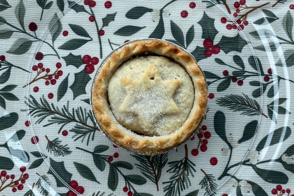 A pie with a star-shaped crust on top sits on a clear plate, placed on a tablecloth with a pattern of green leaves and red berries.