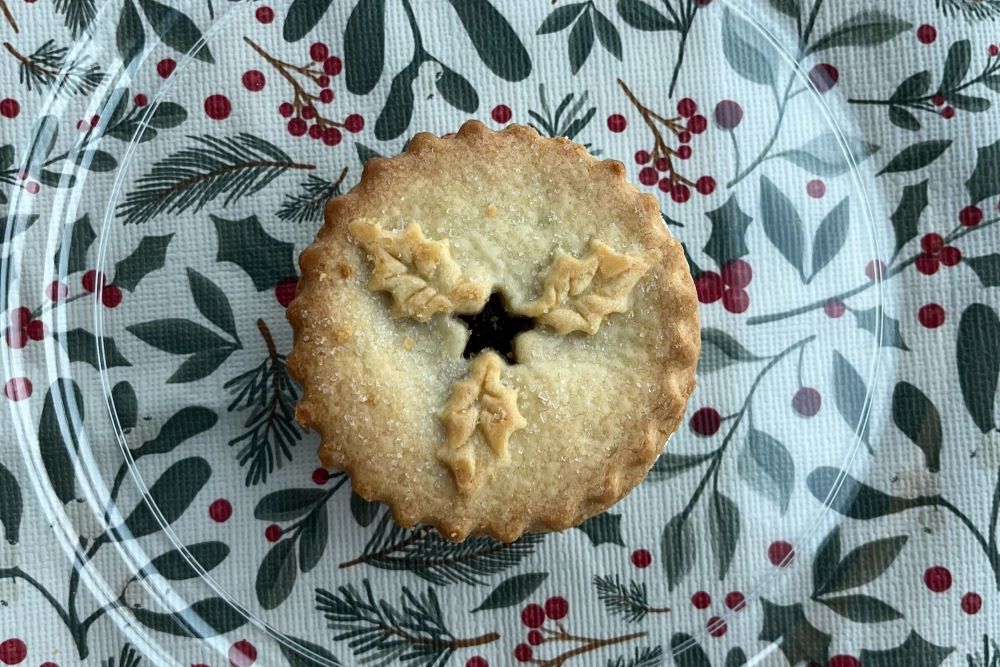 A round pie on a festive cloth with holly berry print, featuring leaf-shaped cutouts on top.