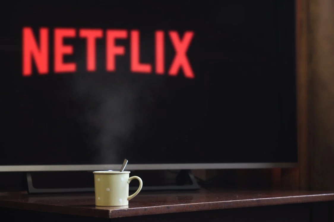 An image showing a mug of coffee in front of a TV showing Netflix, which you can watch without a TV licence