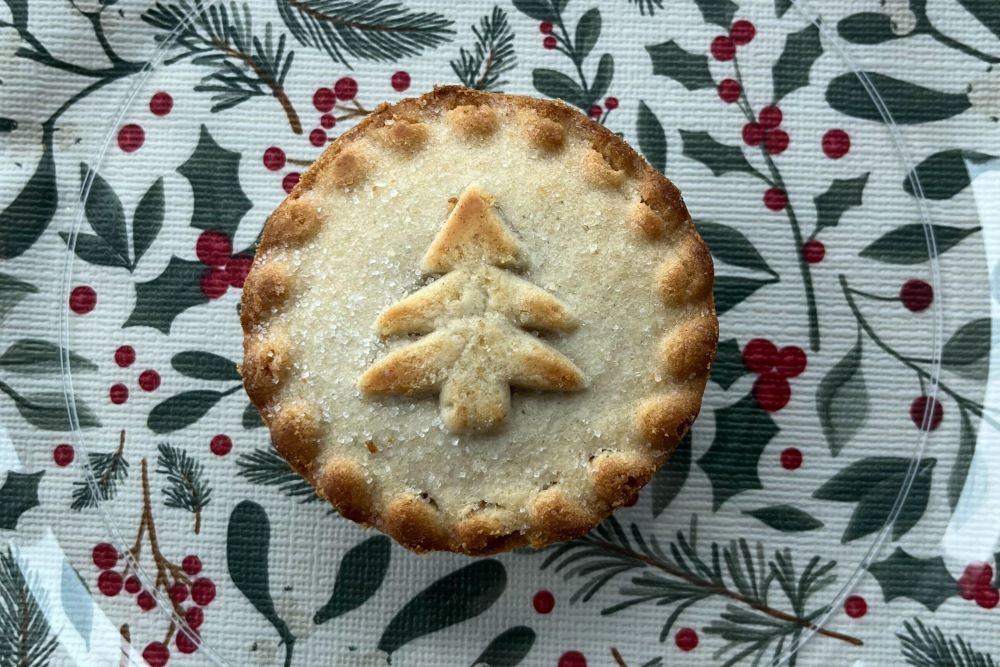 A Christmas-themed pie with a tree-shaped pastry decoration on a festive holly and berry patterned tablecloth.