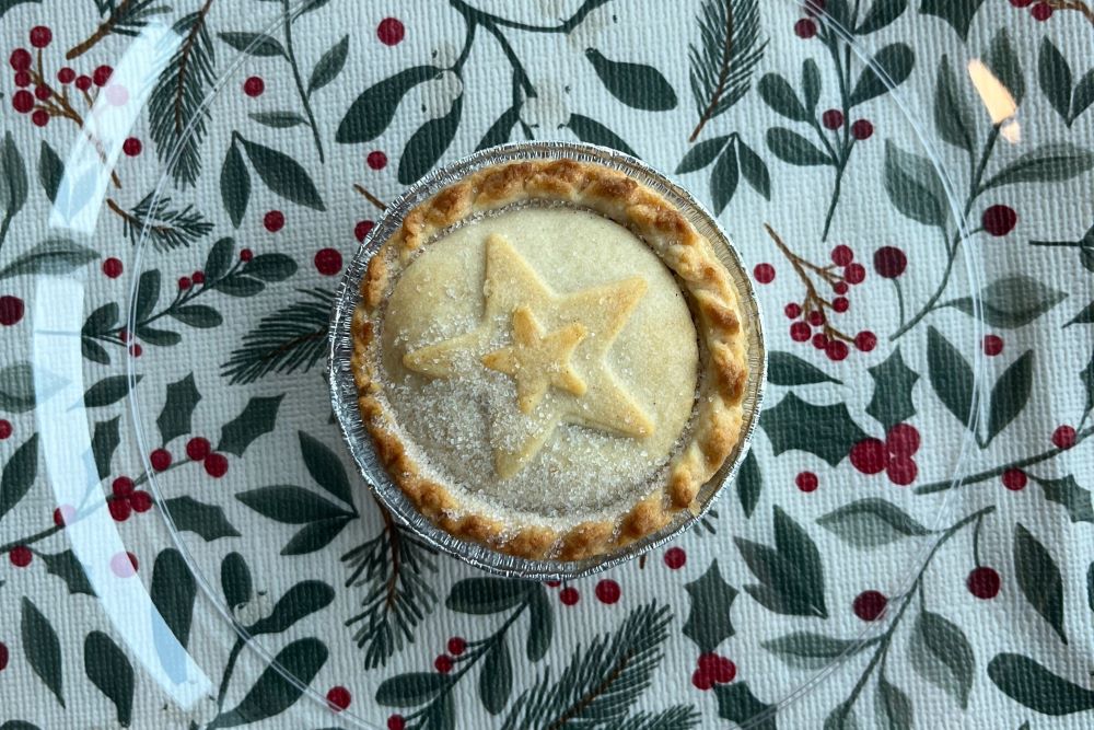 A round pie with a star design on top sits on a festive tablecloth decorated with green leaves and red berries.