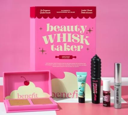 A pink beauty kit box labeled "Beauty Whisk Taker" displayed with various cosmetic products, including compact powder, primer, mascara, tint, and brow gel against a pink background.