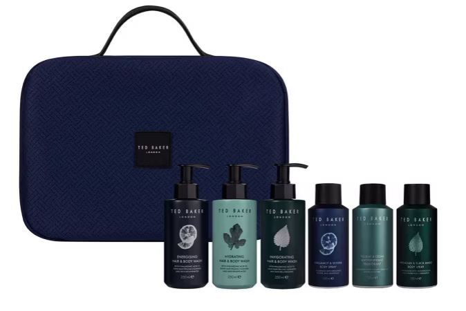 A collection of six Ted Baker grooming products, including hair and body wash bottles, in front of a dark blue carrying case.