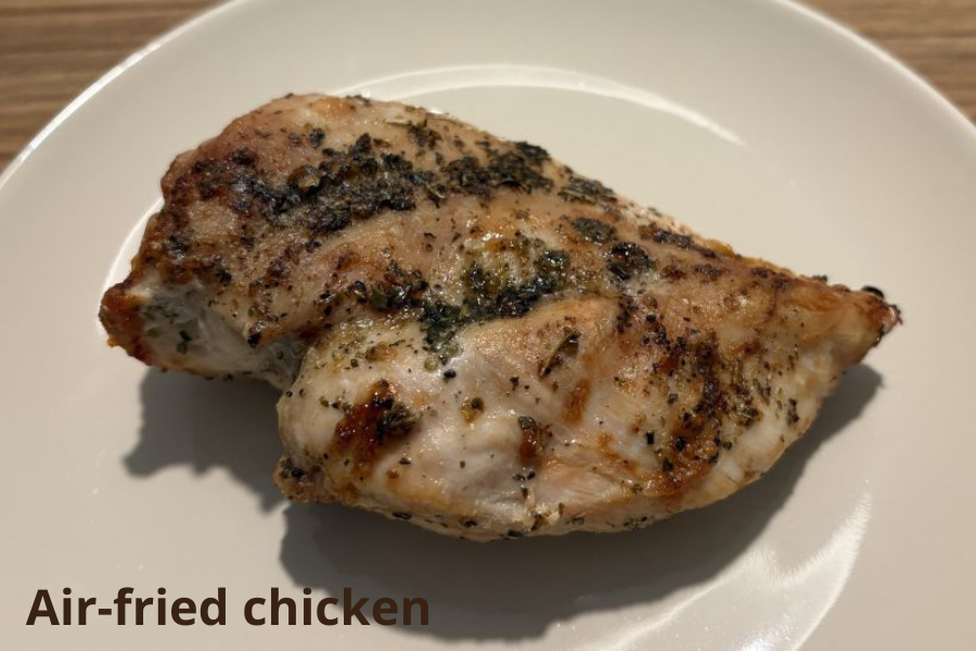 A seasoned piece of air-fried chicken breast is displayed on a white plate.