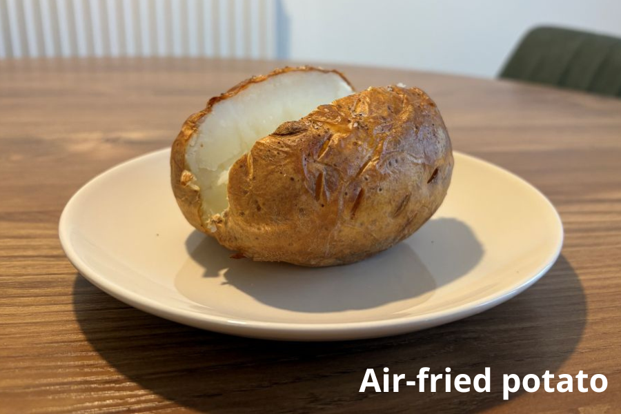 A baked potato on a white plate, placed on a wooden table. The caption reads "Air-fried potato.