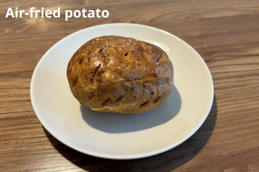 A single air-fried potato on a white plate, placed on a wooden surface.