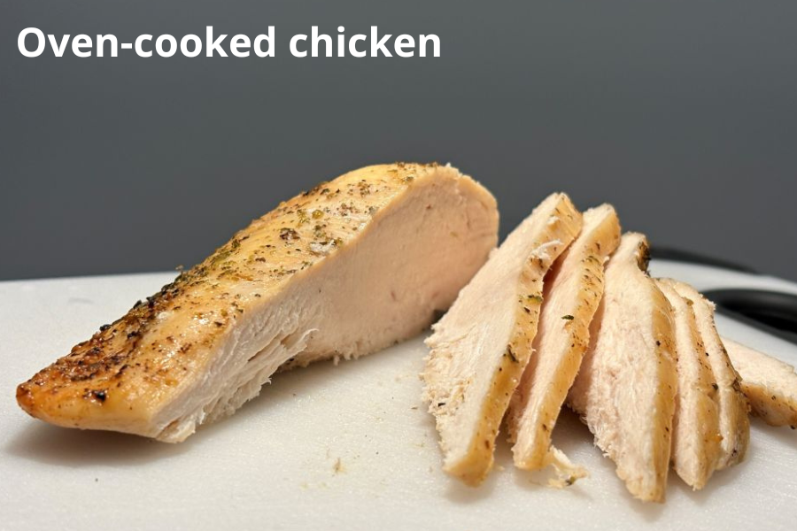 Sliced oven-cooked chicken breast on a cutting board, seasoned with herbs.