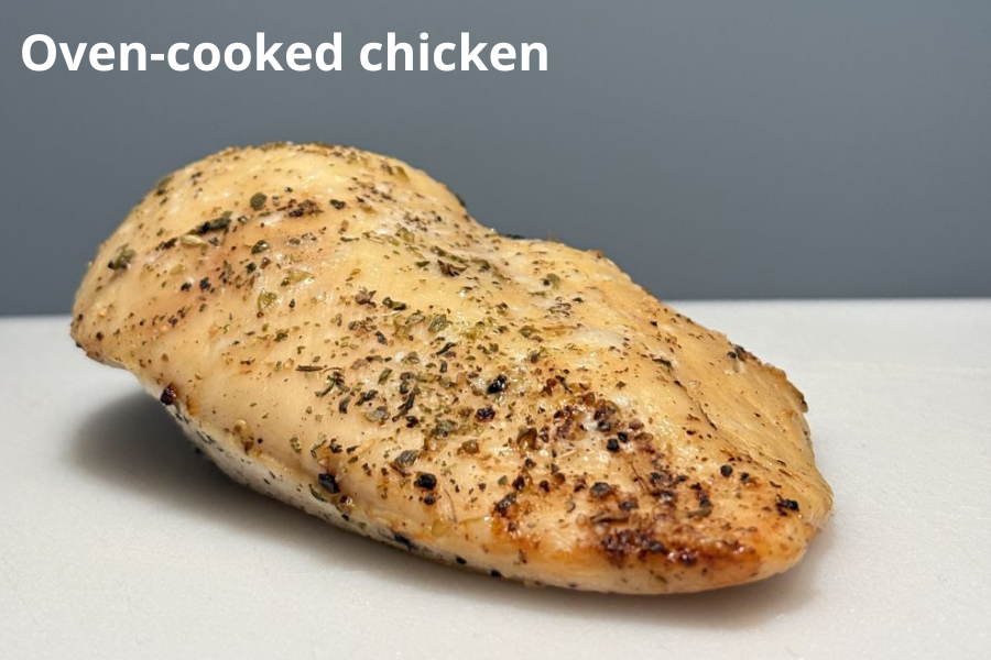 A seasoned piece of oven-cooked chicken rests on a white surface against a plain gray background.