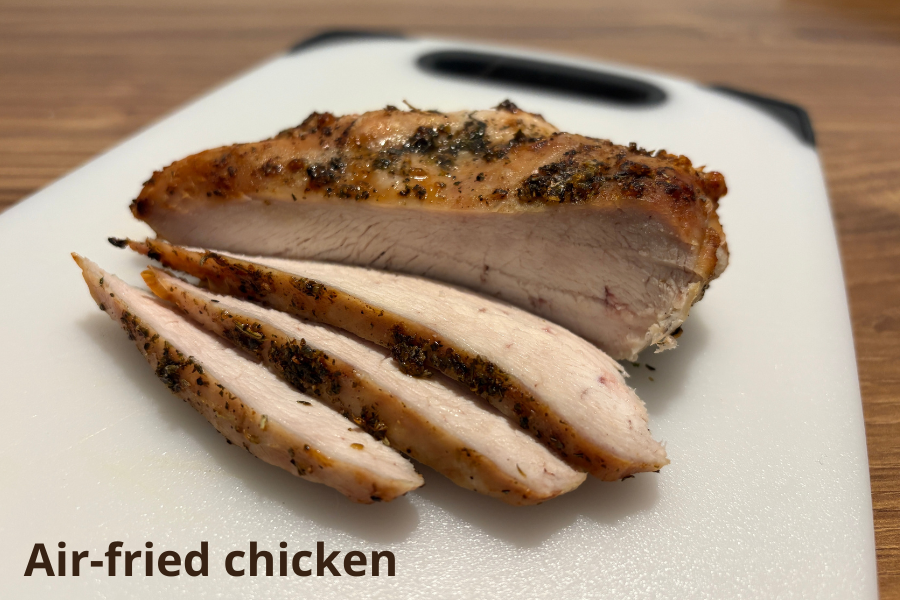 Sliced air-fried chicken breast seasoned with herbs on a white cutting board.