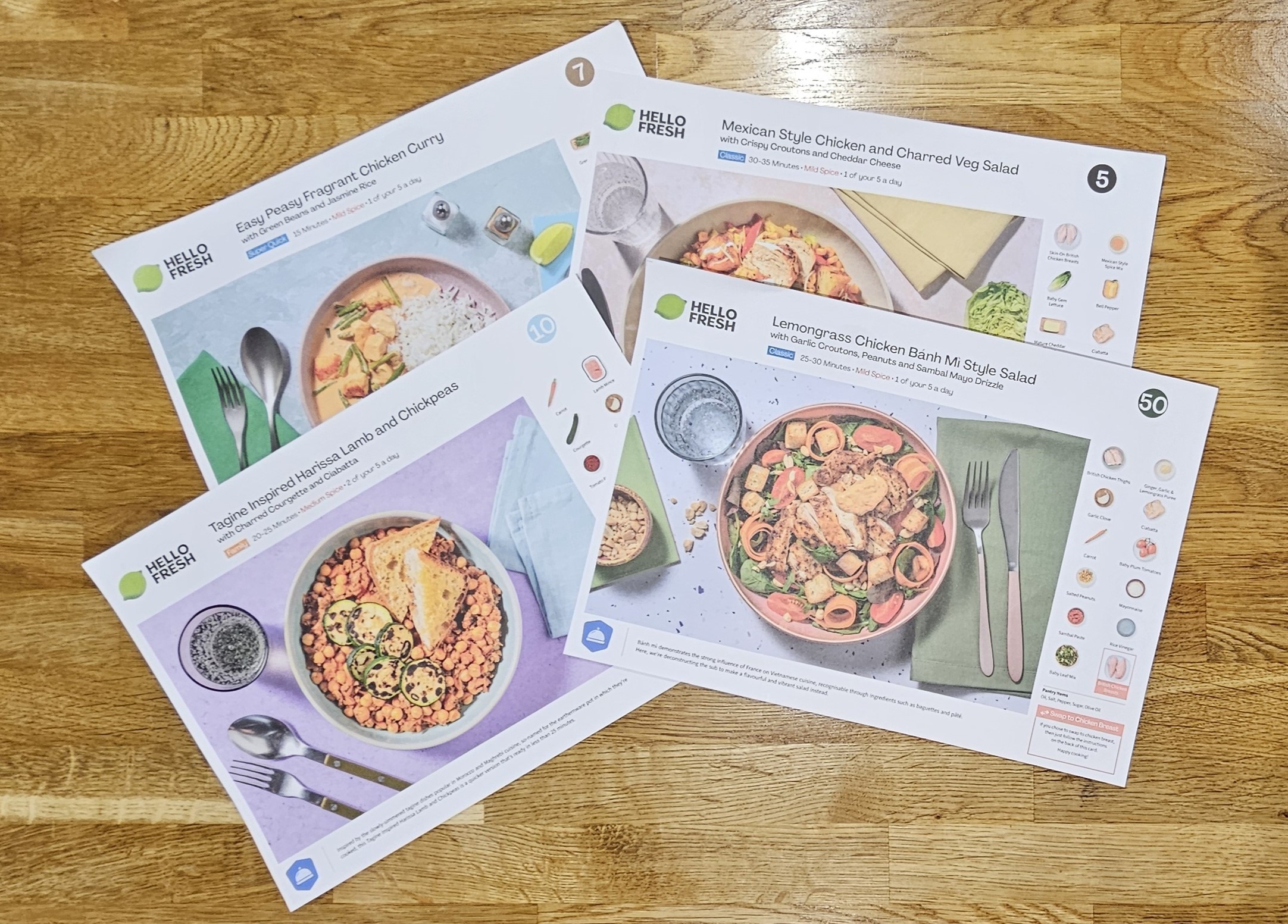 Three HelloFresh recipe cards on a wooden surface, including options for curry, Mexican-style chicken salad, and a lemongrass chicken bahn mi salad.