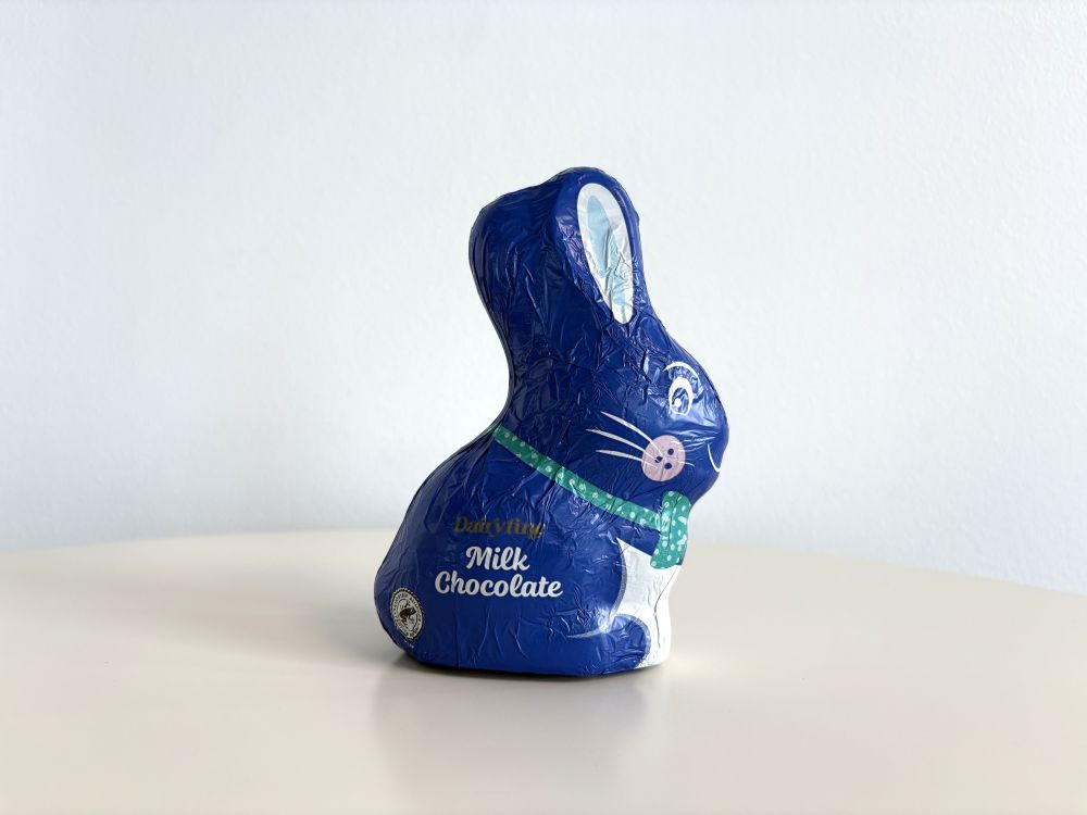 Foil-wrapped milk chocolate bunny with a blue covering, sitting on a white surface.