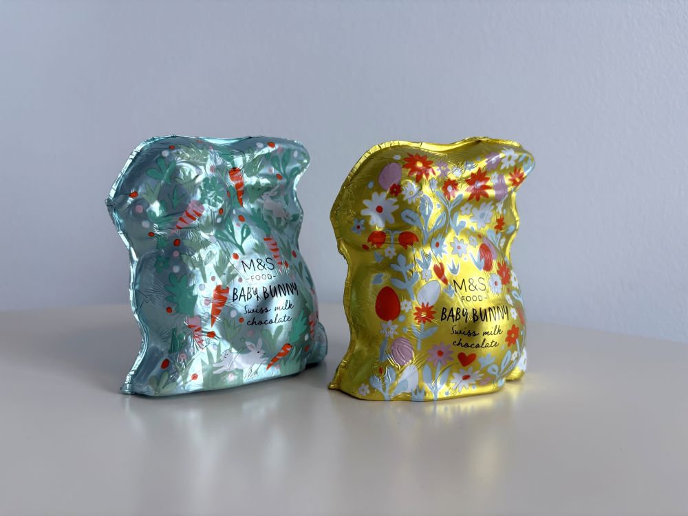 Two decorative foil-wrapped chocolate packages are displayed on a surface. One is blue with floral designs, and the other is yellow with a similar pattern.